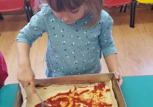 Dzieci smarują spód pizzy sosem pomidorowym.